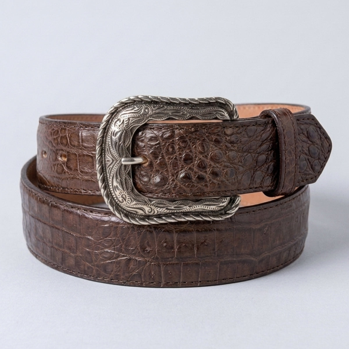A Los Altos men's brown caiman hornback leather belt with a silver-toned western-style buckle, coiled on a light gray background.