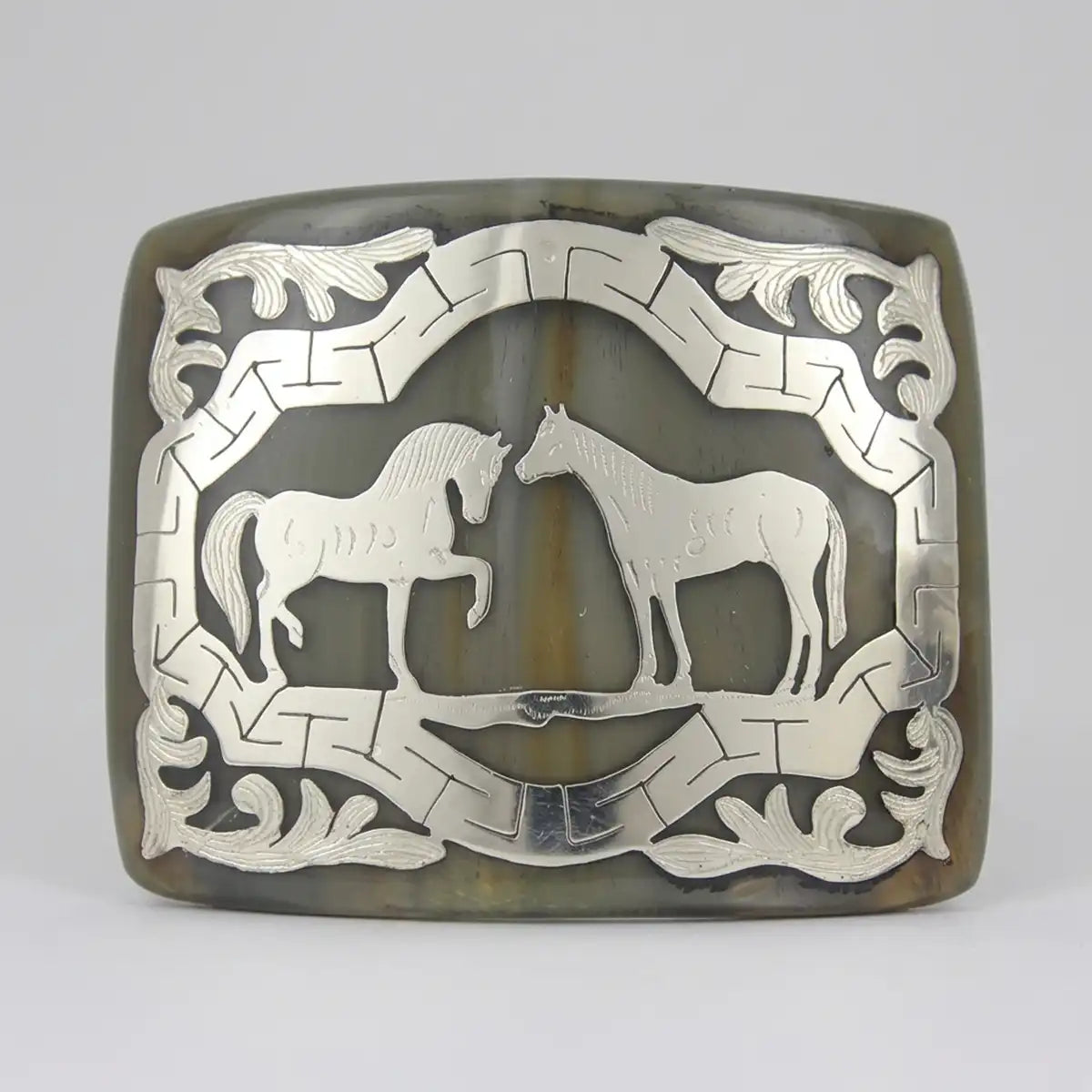 Studio view of the genuine bull horn belt buckle with metal two horses inlay and geometric ribbon frame.