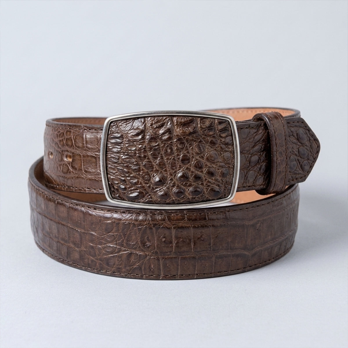 A Los Altos men's brown crocodile hornback leather belt with a silver-toned rectangular buckle, coiled on a light gray background.