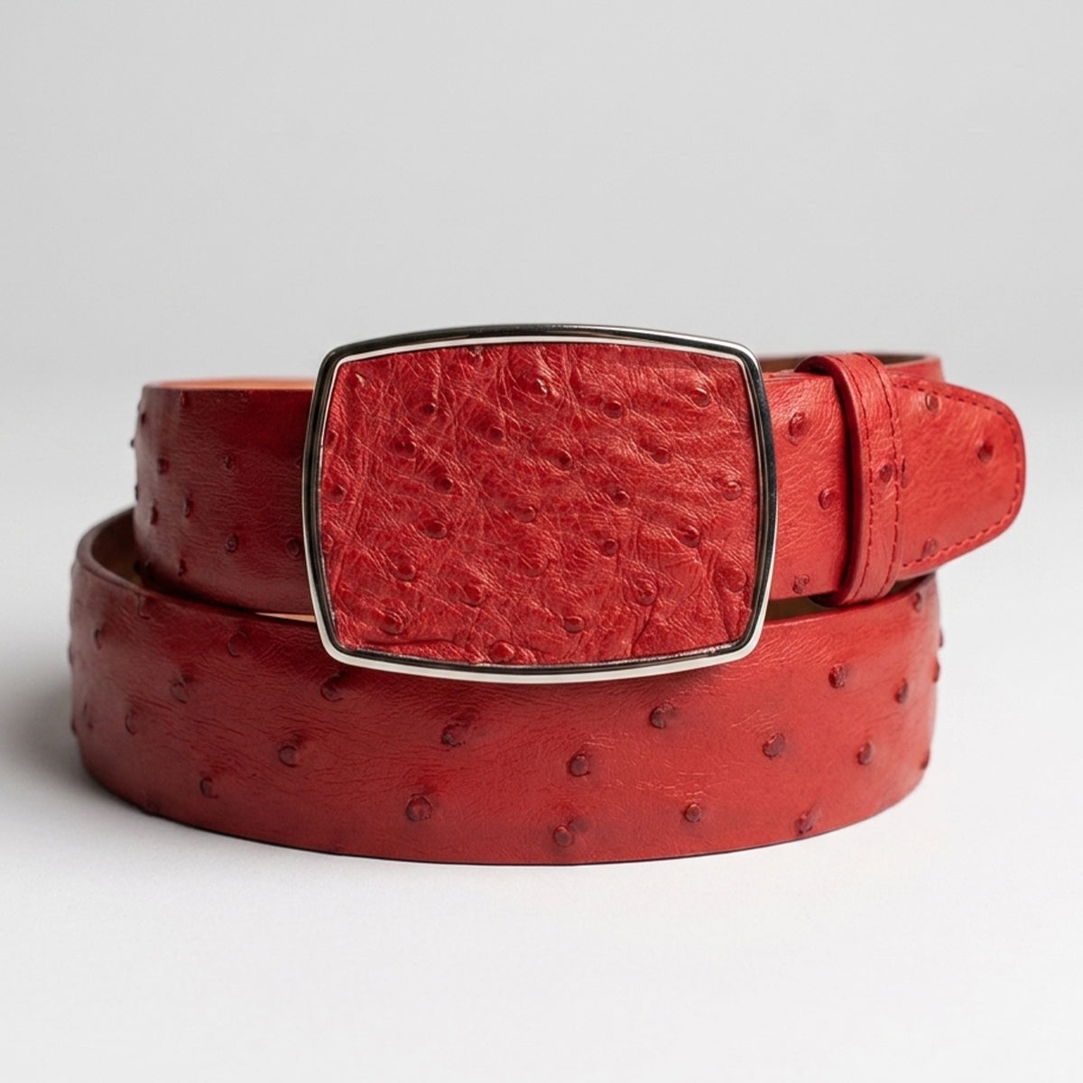 Los Altos men's red ostrich leather belt with a textured rectangular buckle, coiled on a light gray background.