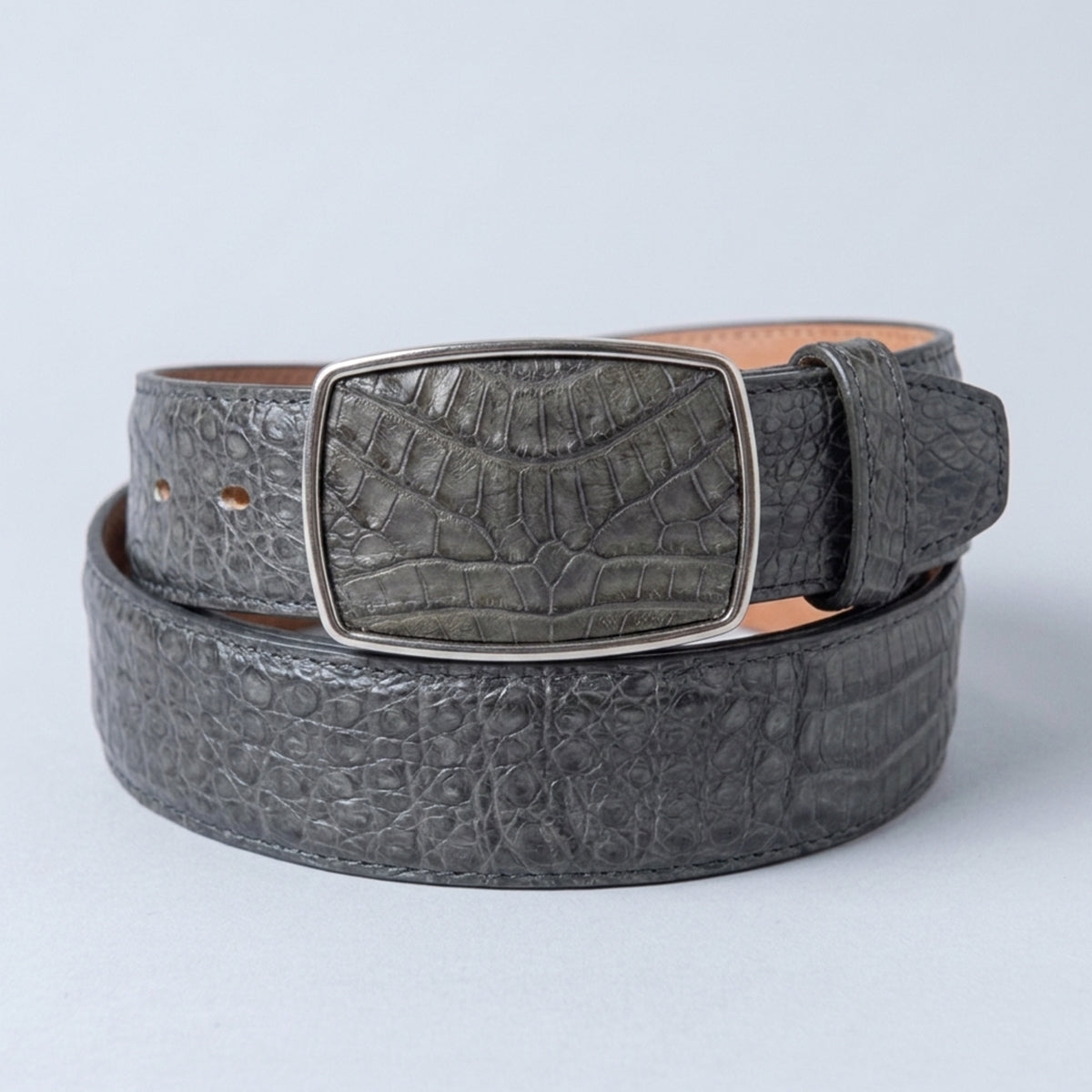 A dark gray crocodile belly leather belt with a rectangular silver-tone buckle on a light gray background.