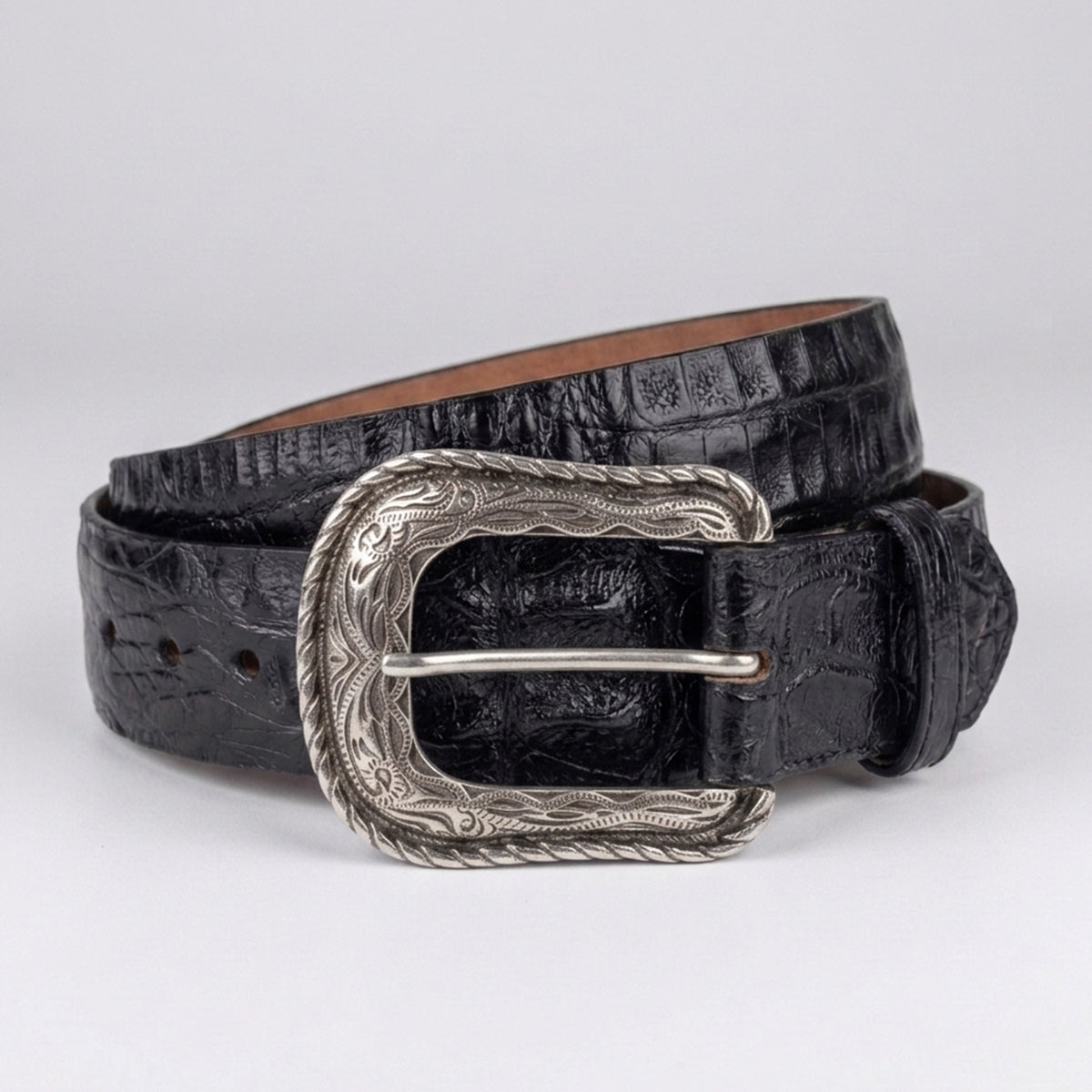 A black crocodile-embossed leather belt with a silver-toned western heel-bar buckle, coiled on a light gray background.