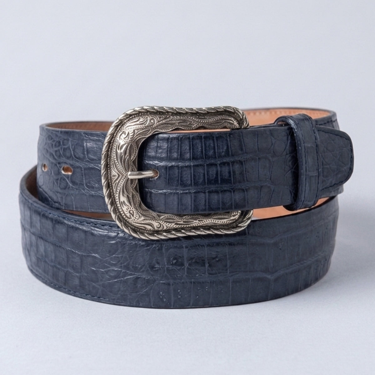 A dark navy blue caiman belly leather belt with a silver-tone western heel-bar buckle, coiled on a light gray background.