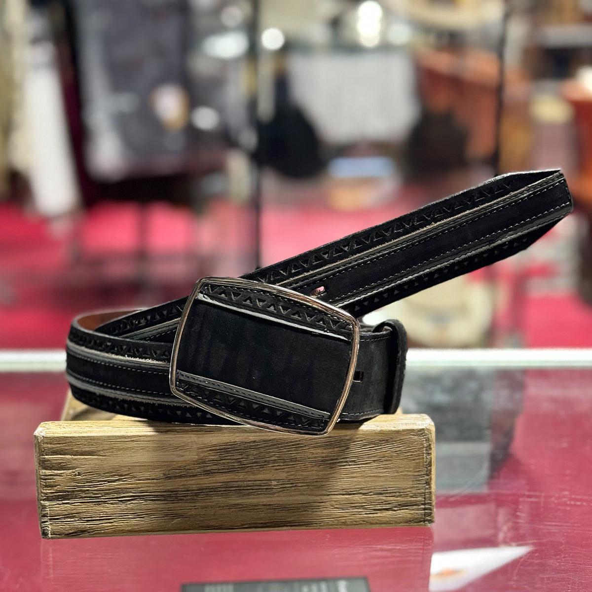 Los Altos men's black suede leather belt with a decorative buckle on a wooden stand against a blurred background.