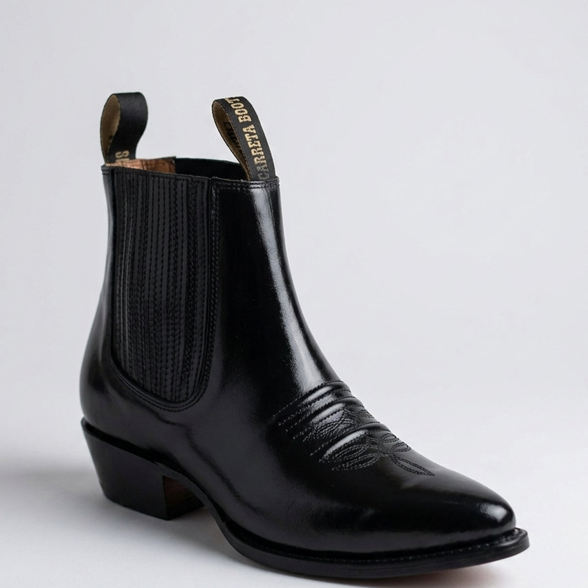 Carreta men's high-shine black leather Western ankle boot featuring elastic side gore panels, pointed toe, and underslung Cuban heel.