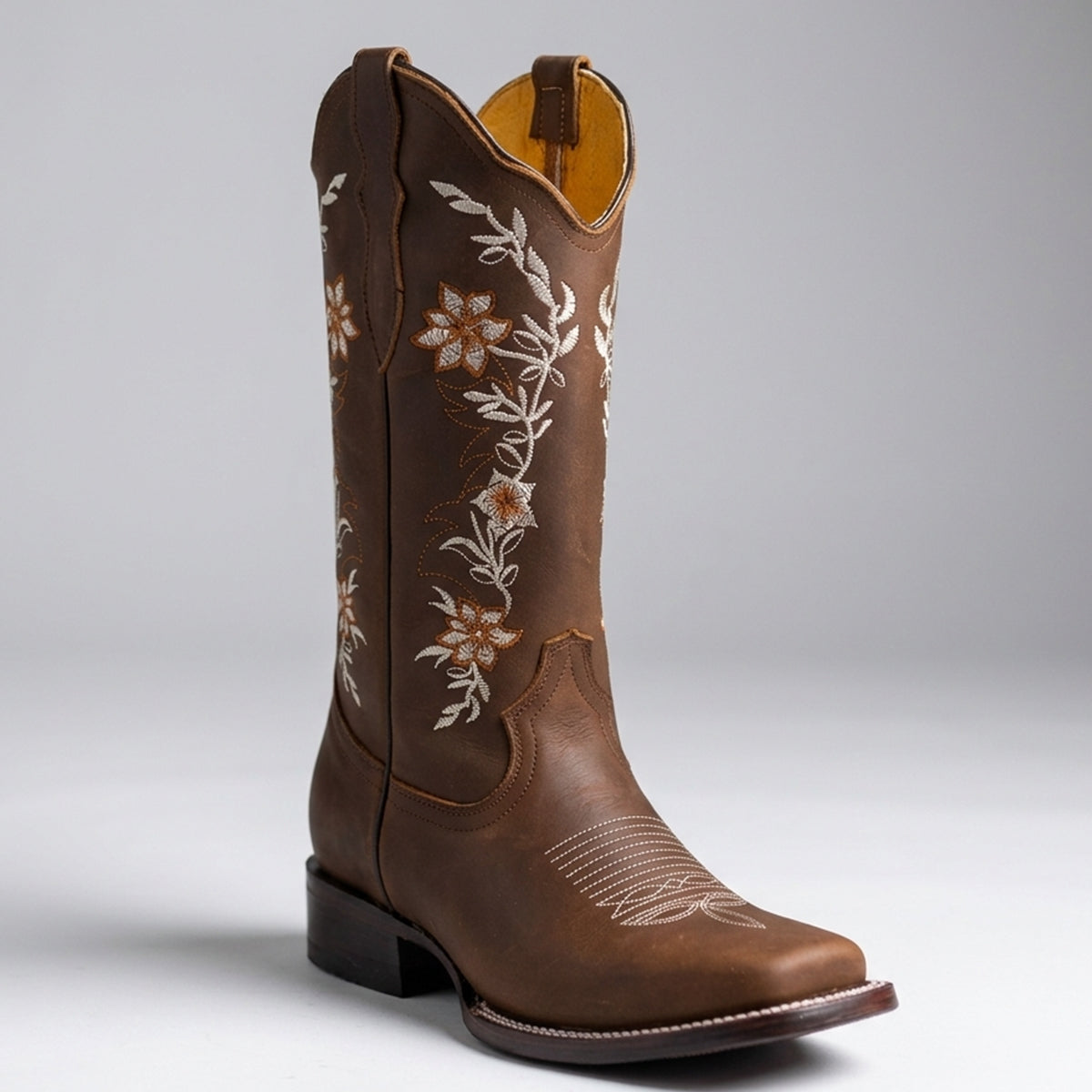 La Sierra women's leather cowboy boot with white floral embroidery on the shaft, a square toe, and a low stacked heel, photographed on a light gray studio background.