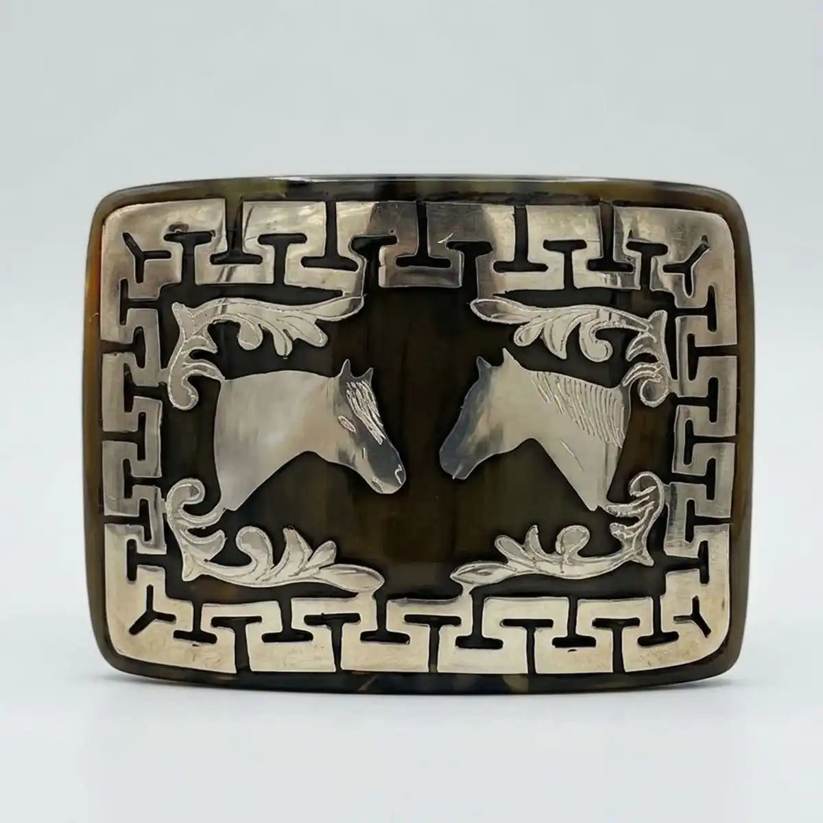 Studio white background product photo of the genuine bull horn belt buckle with metal twin horse heads inlay and geometric frame.