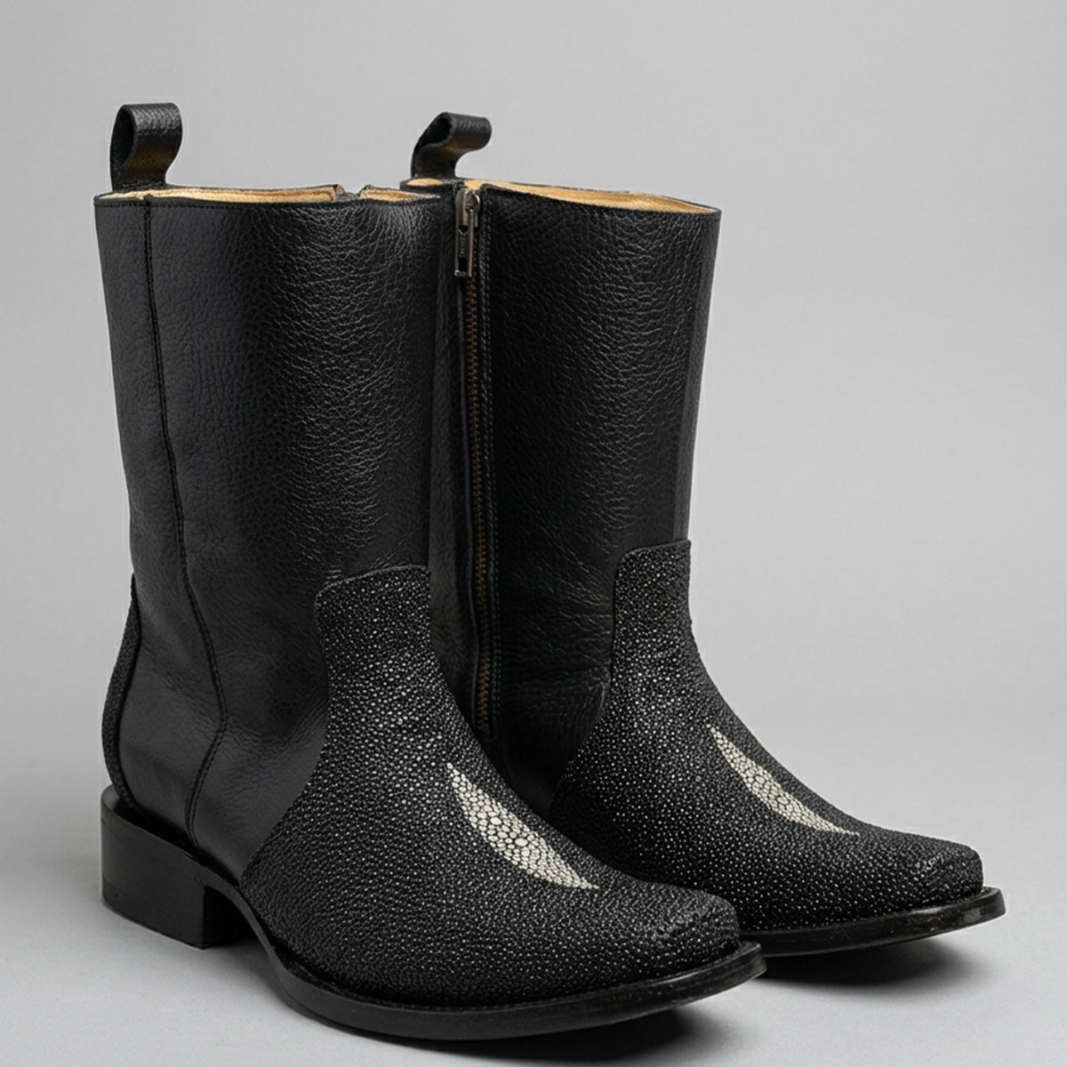 A pair of black leather cowboy boots with a textured stingray print, side zippers, and pull tabs, shown against a neutral gray background.