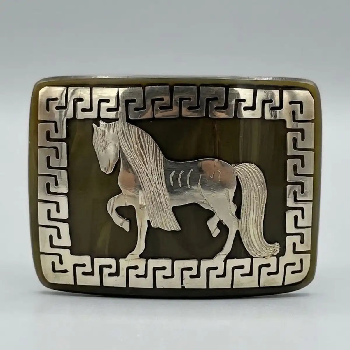 Studio white background product shot of the genuine bull horn belt buckle featuring a metal prancing horse inlay and Greek key border frame.
