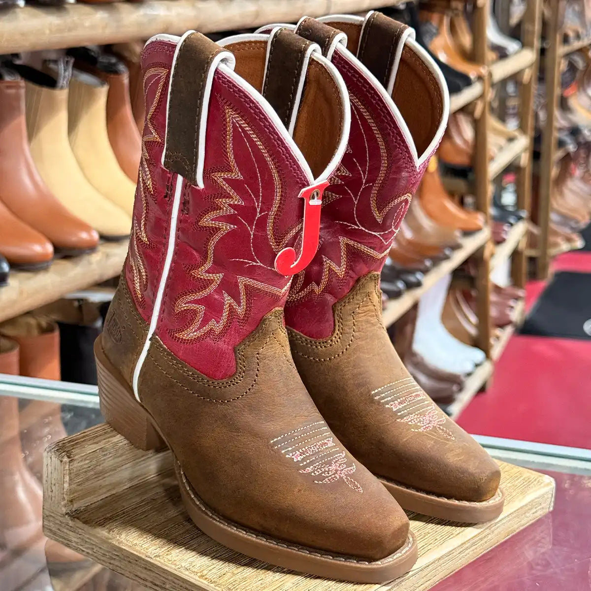 In-store display view of the Justin Kids' Whinny Junior brown and red water buffalo leather cowboy boots showing the snip toe and red tag.