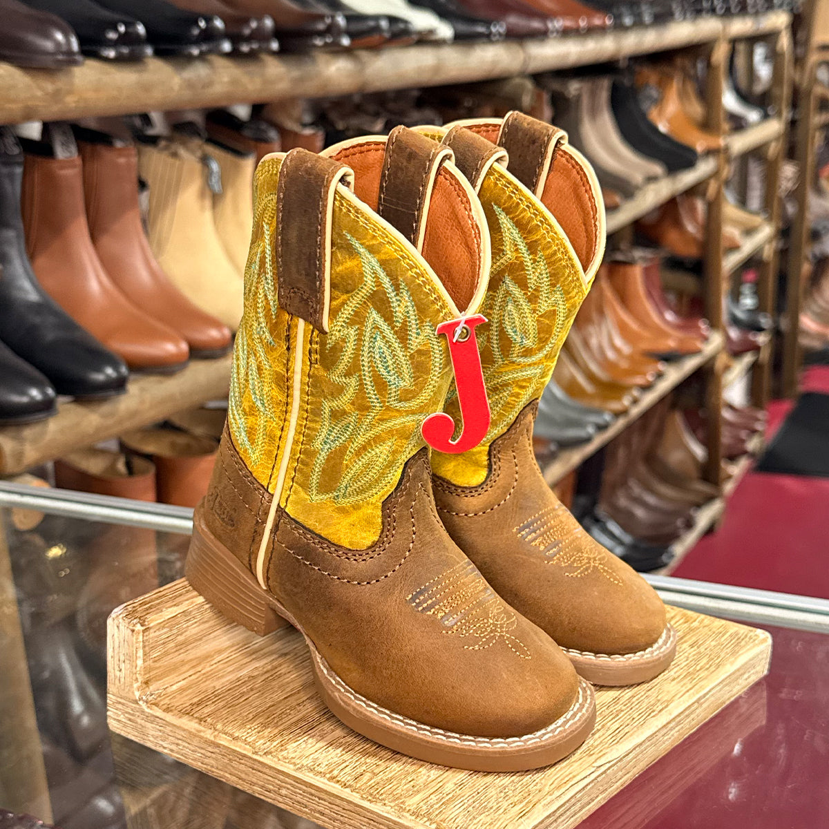 Pair of Kids Justin brown cowboy boots with yellow lining on a wooden stand in a shoe store.