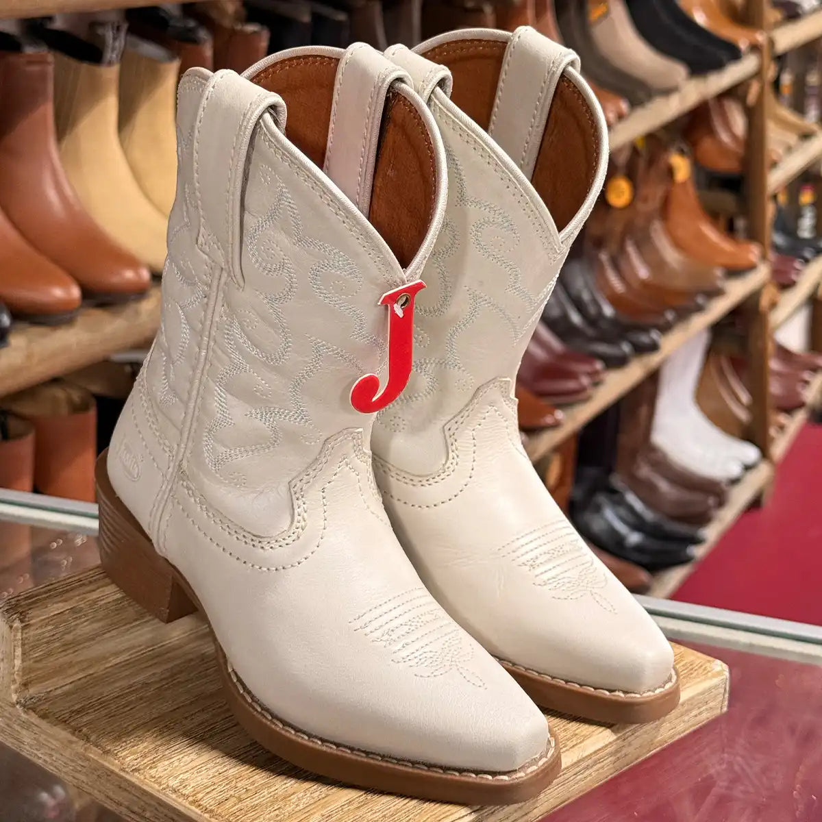 In-store counter display view of the Justin Kids' white Bronci boots with red 'J' branding tag.