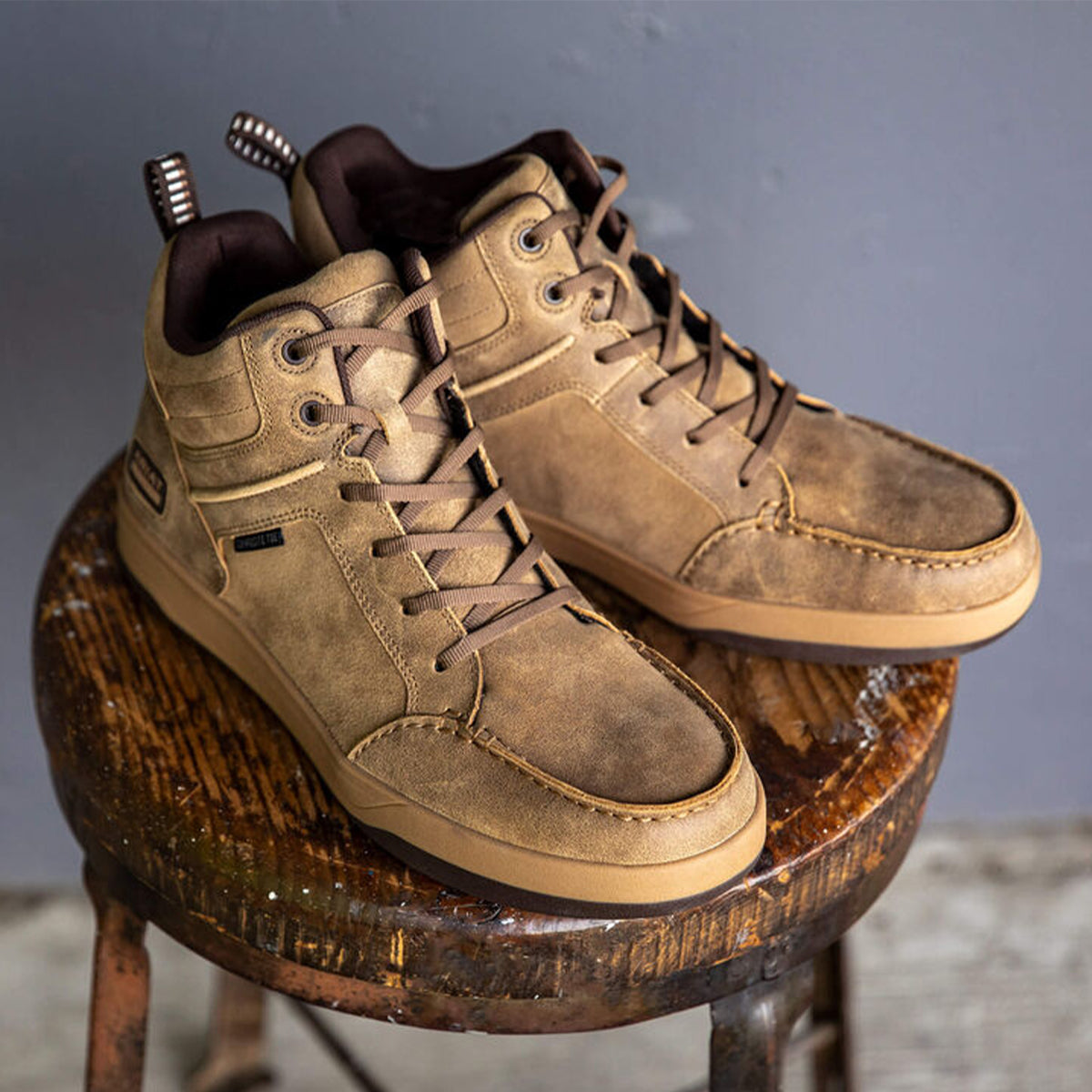 Pair of Ariat outmatch brown high-top sneakers on a wooden stool against a gray background.