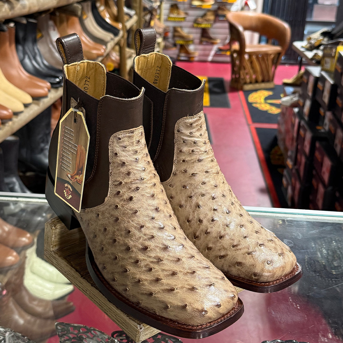 In-store display view of Los Altos men's exotic full-quill ostrich Chelsea boots featuring a natural beige ostrich leather foot, dark mocha brown elastic side gores, pull tabs, and a modern square toe profile.