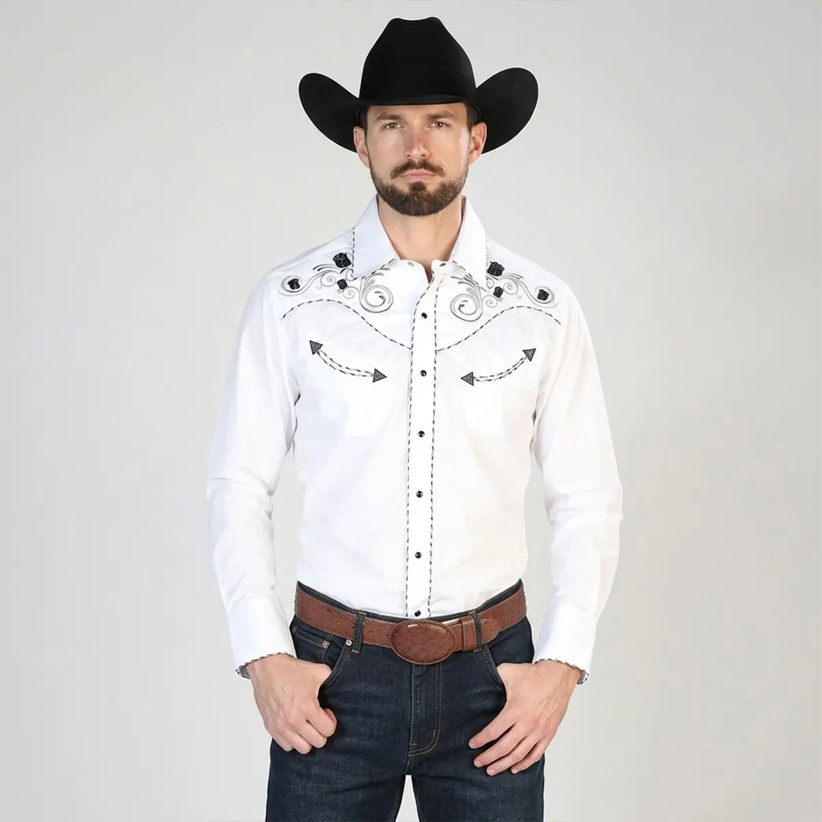 Front cropped view of a male model wearing a white traditional embroidered Western snap shirt featuring black rose shoulder embroidery, contrast stitching, and an ostrich leather belt with dark trousers.