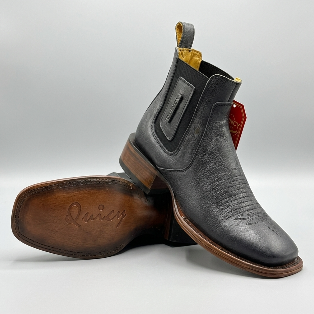A pair of black leather Chelsea boots with a pull tab and elastic side gore, shown with one boot standing upright and the other lying on its side to display the sole. The brand name 'Quincy' is embossed on the sole and visible on the side tag.