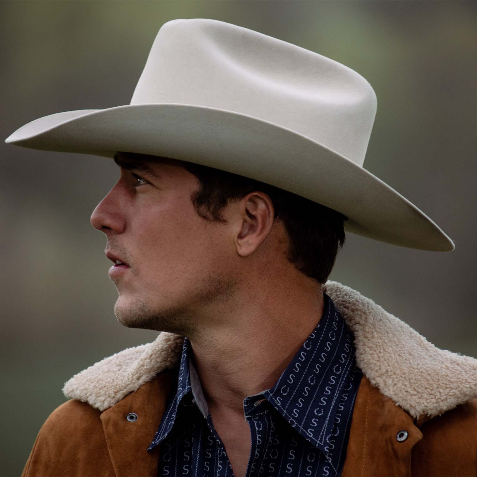 Man wearing a Stetson cowboy hat and brown leather jacket with a blurred background