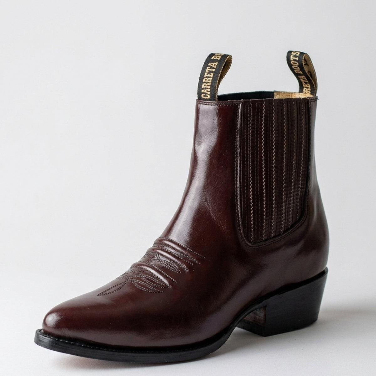 A dark brown leather ankle boot with elastic side panels and a black heel, shown from a three-quarters angle on a light gray background.