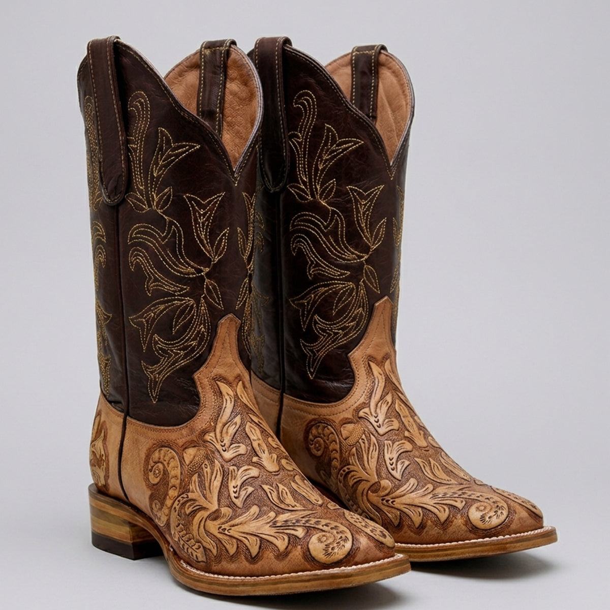 A pair of men's western cowboy boots in brown leather with intricate floral tooling and embroidery on the shafts and toes, shown against a neutral gray background.