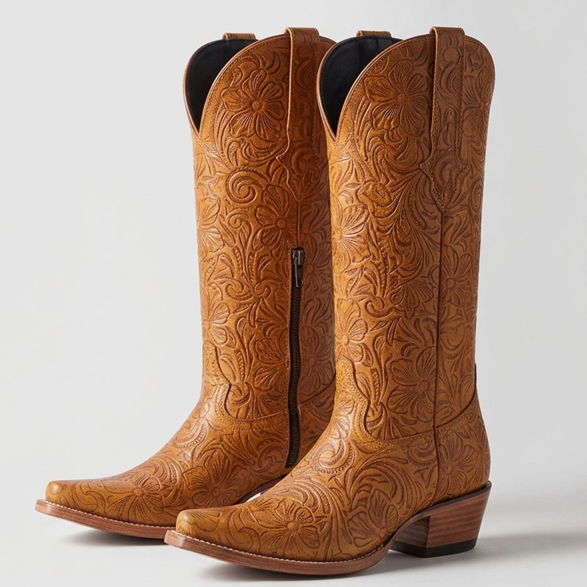 Women's tan leather tall cowboy boots featuring an all-over floral tooled print pattern, snip toe, inside ankle zipper, and stacked leather heel.