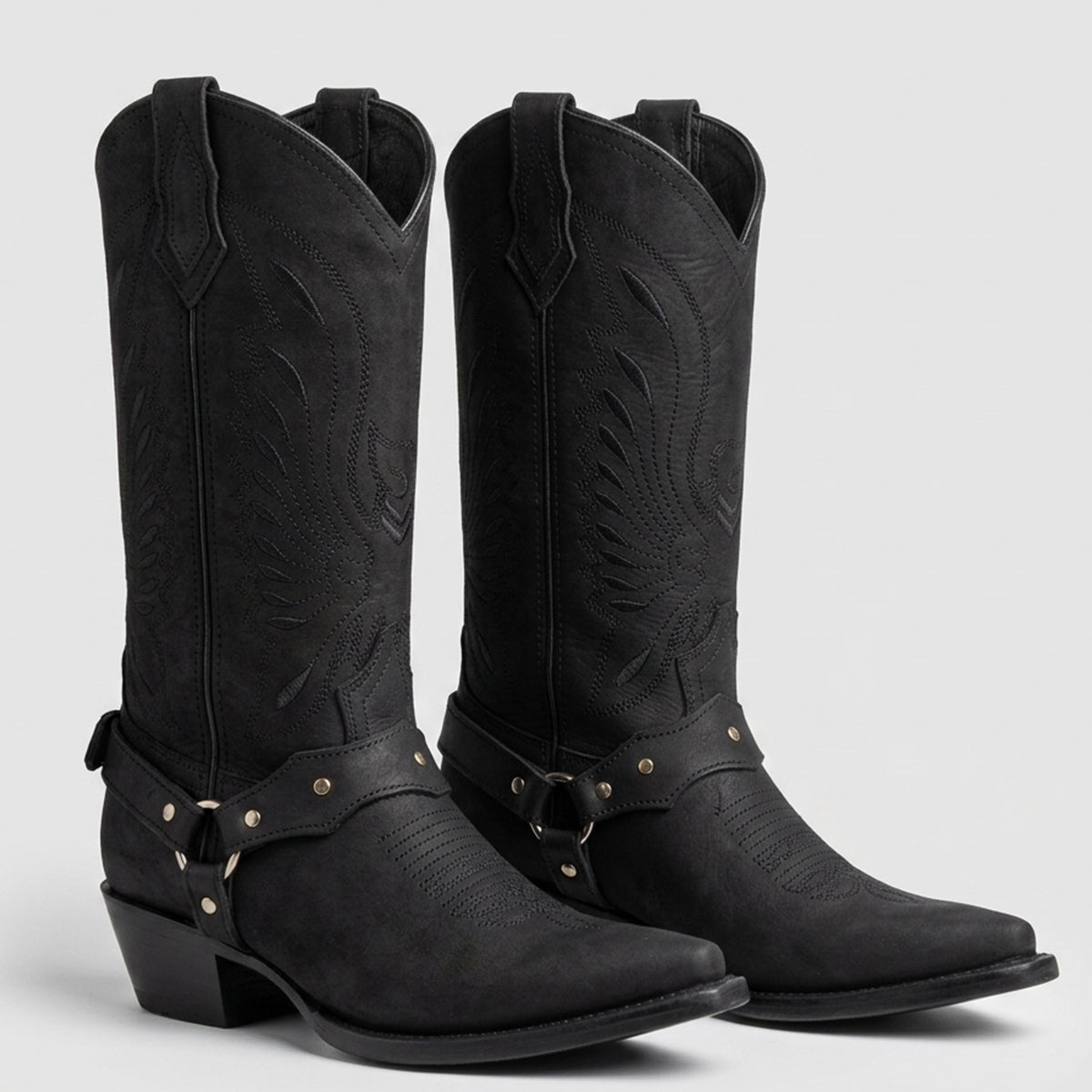 Pair of La Sierra black matte leather cowgirl boots with pointed toes, studded harness straps, and subtle Western embroidery on the shaft.