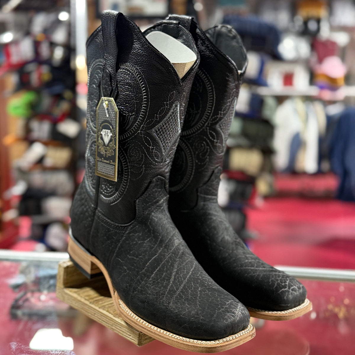 Pair of bull shoulder leather black cowboy boots on display with a blurred store background.
