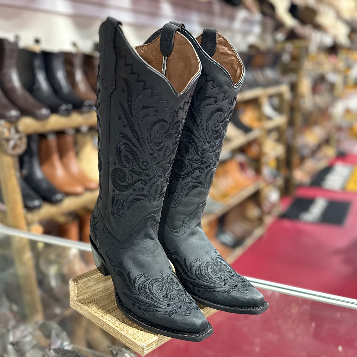 Corral women's cowgirl boots with intricate designs on a wooden block in a store setting.