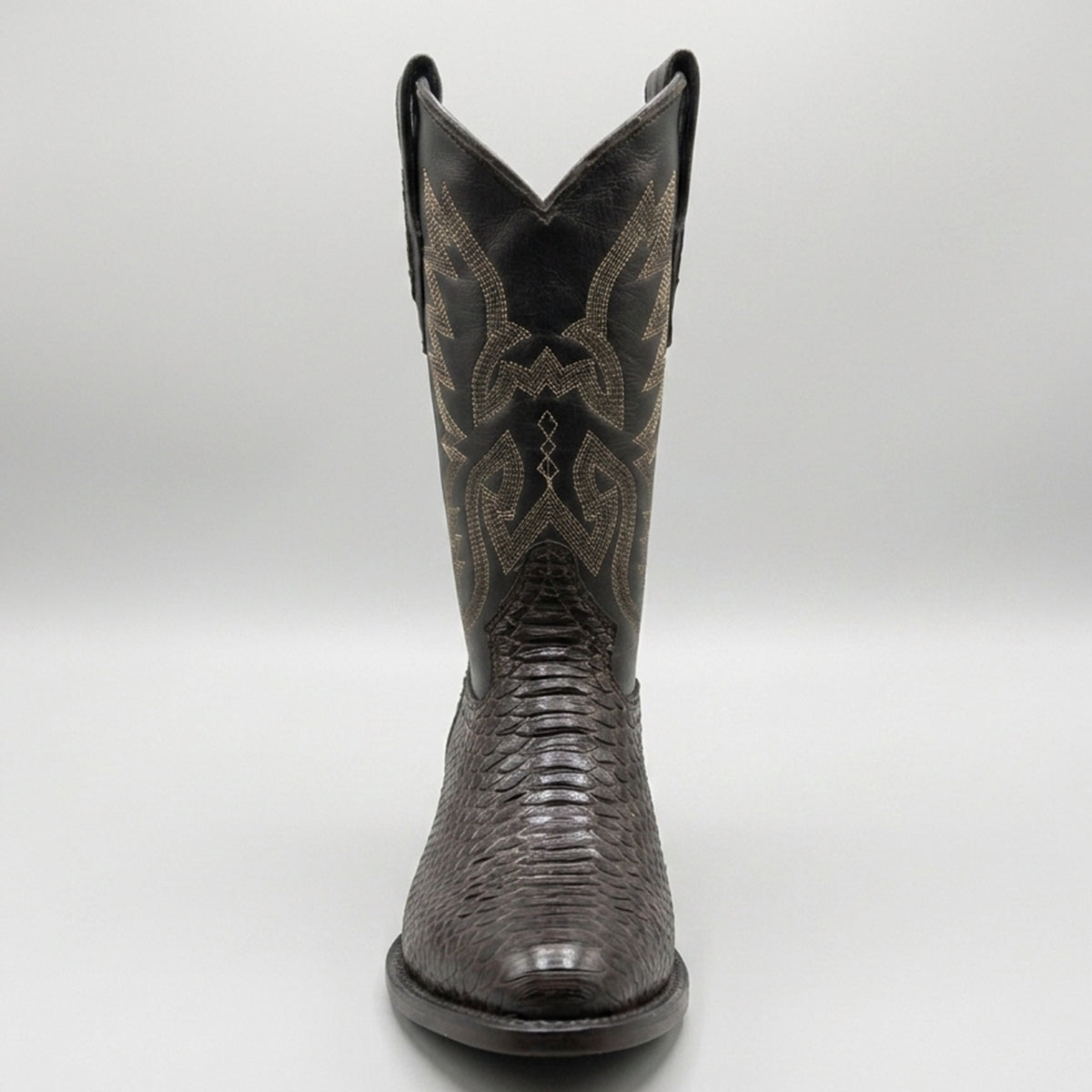 A single dark brown western cowboy boot with a textured python-embossed foot and a black shaft featuring tan embroidered stitching, shown against a neutral gray background.
