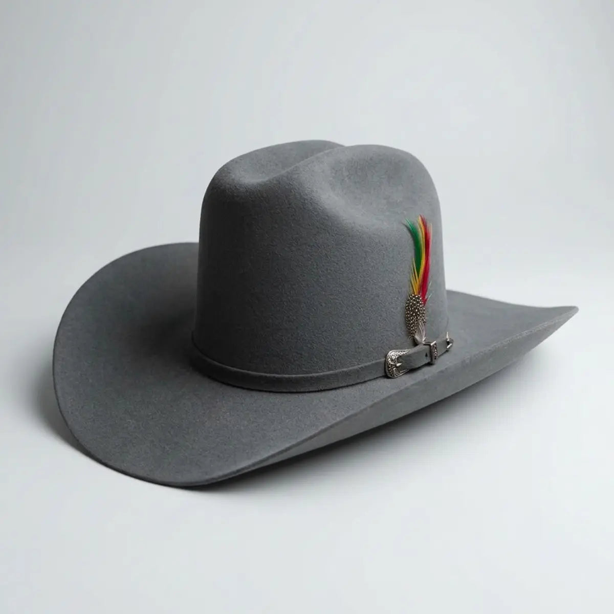 Three-quarter studio profile view of the Abolengo Rancheron 1000X grey rabbit fur felt tejana hat displaying the 5-inch Cattleman crown crease, Sinaloa brim, silver buckle set, and feather accent.
