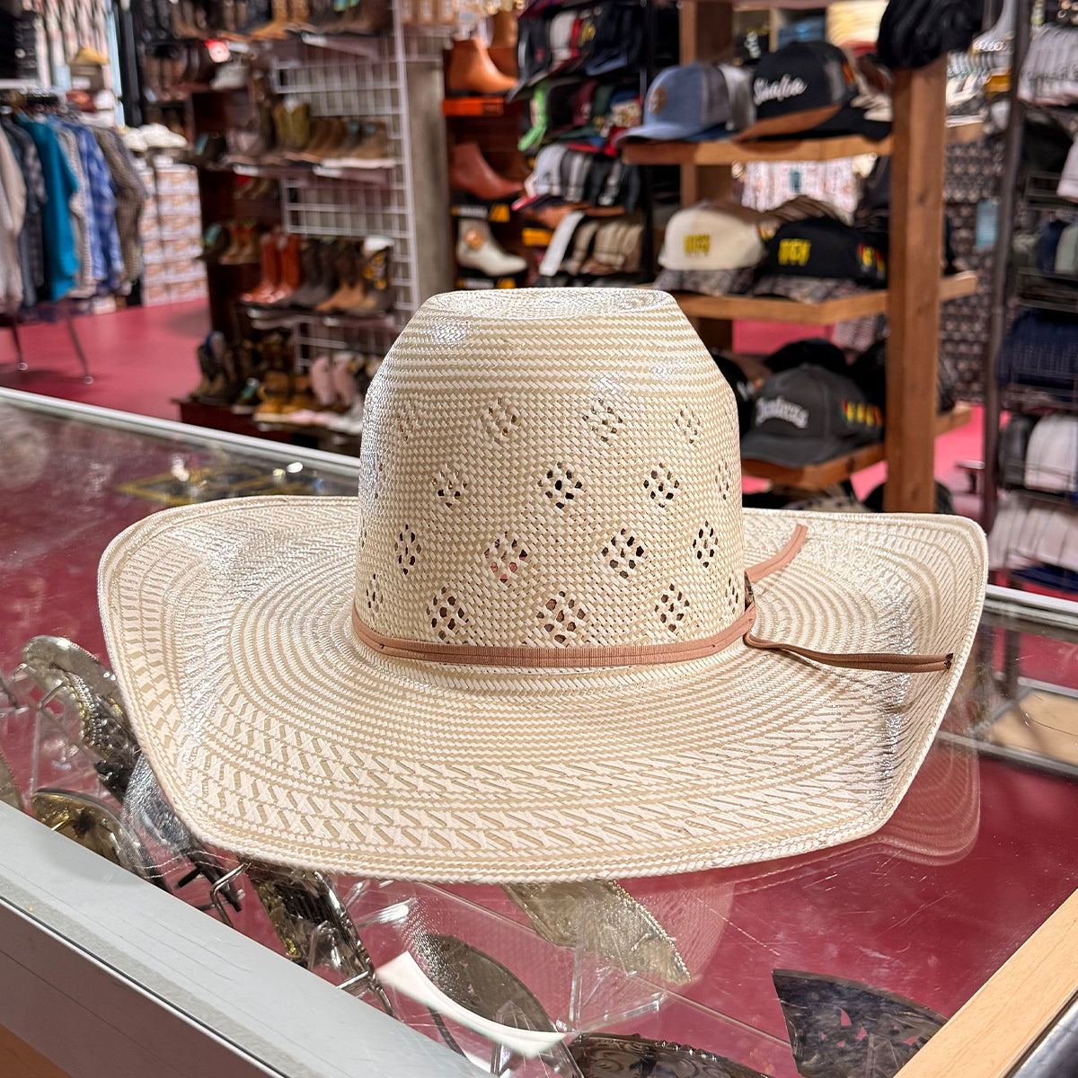 American Hat Company straw cowboy hat with a light tan band, displayed on a glass counter inside a retail store.