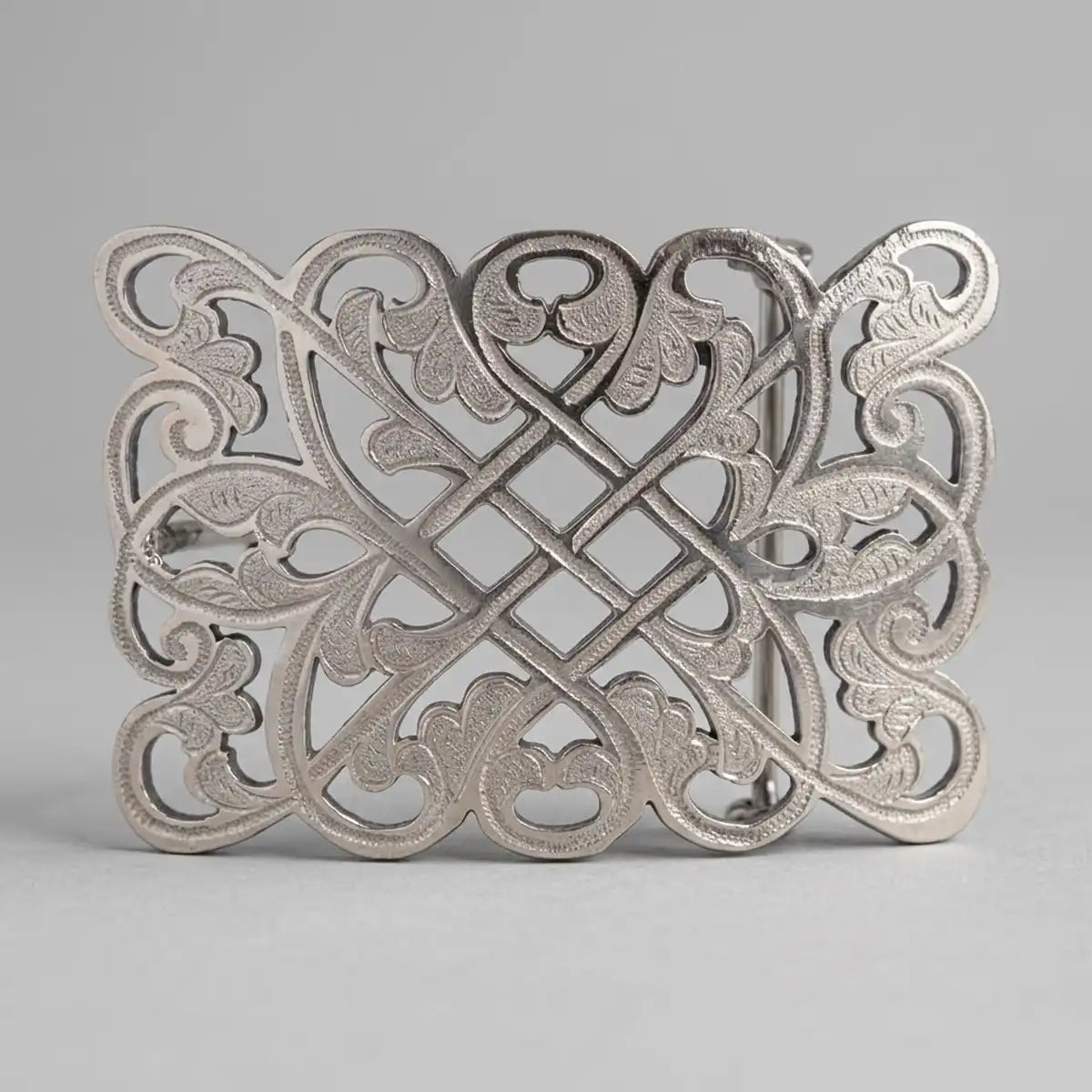 An ornate silver-toned metal belt buckle featuring an intricate Celtic knot design with leaf and scroll motifs, photographed on a neutral gray background.