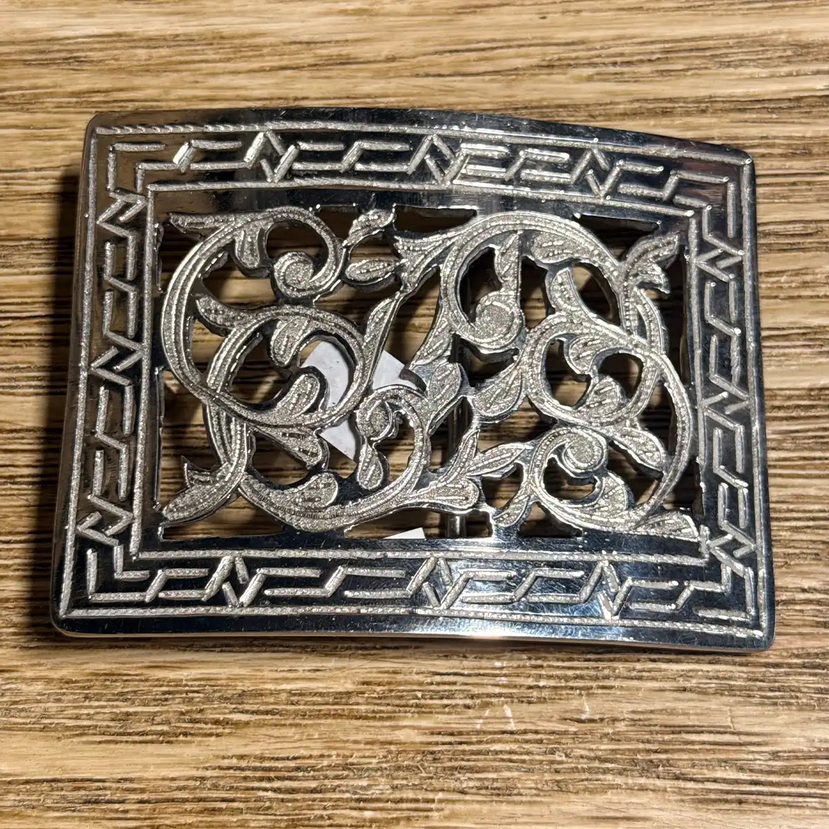 In-store display view of the 4" x 3" stainless steel cutout belt buckle resting on a wooden counter top.