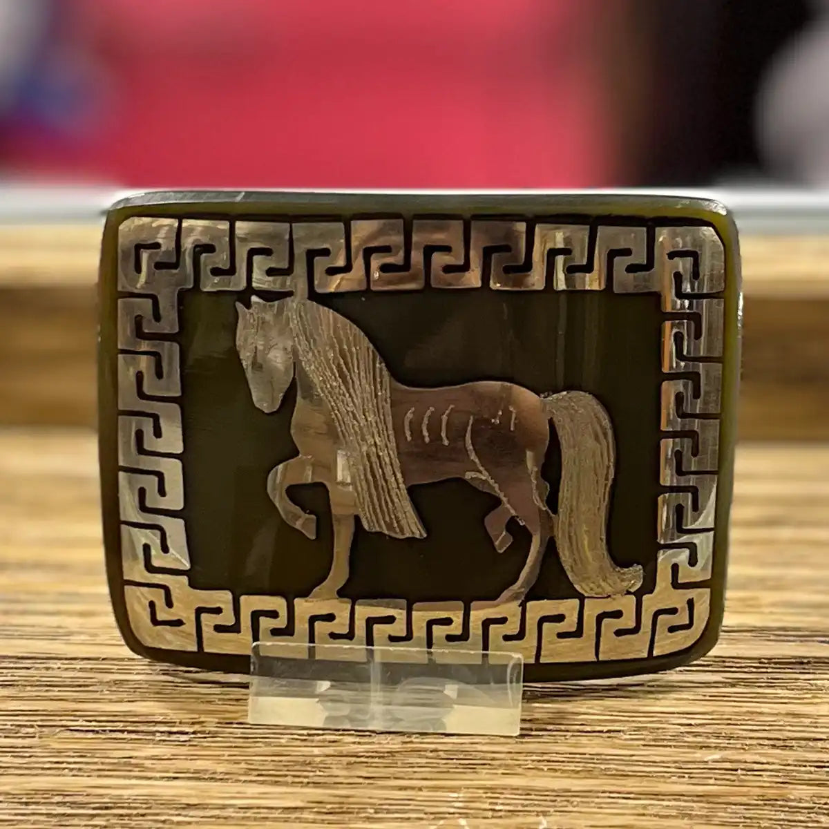 In-store counter display view of the handcrafted genuine bull horn western belt buckle showing the prancing horse inlay on an acrylic stand.