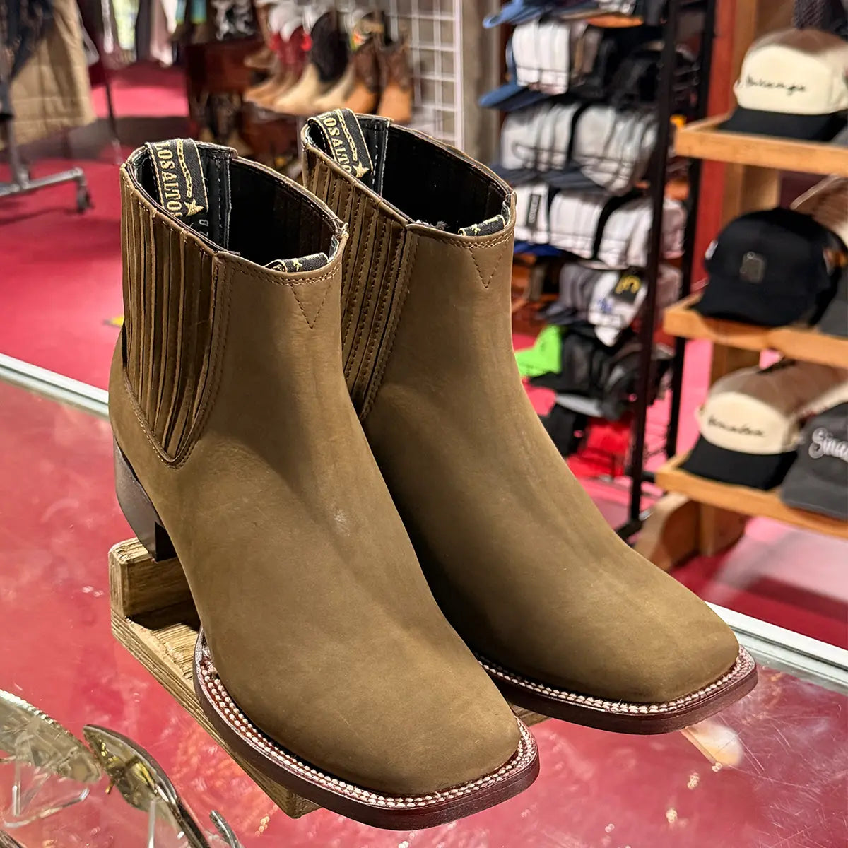 In-store display view of the Los Altos men's brown nubuck Chelsea boots resting on a glass counter highlighting the branded pull straps and ankle collar.