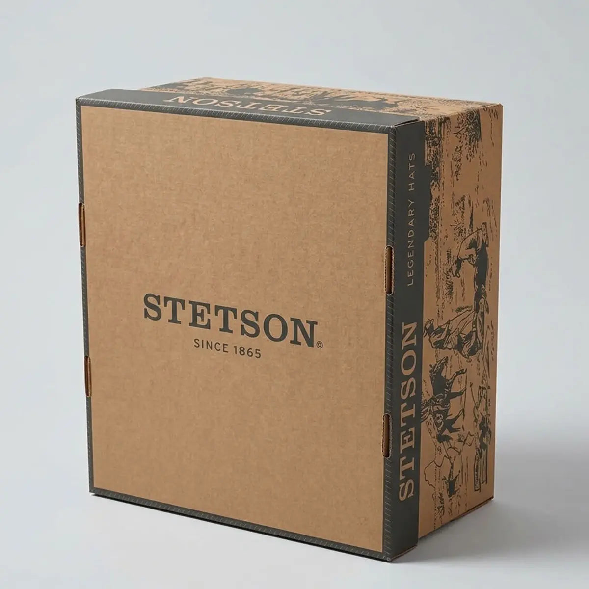 Three-quarter studio view of the signature Stetson brand cardboard box in natural brown Kraft with dark grey paneling and vintage Western illustrations, featuring "STETSON SINCE 1865" printed on the front.