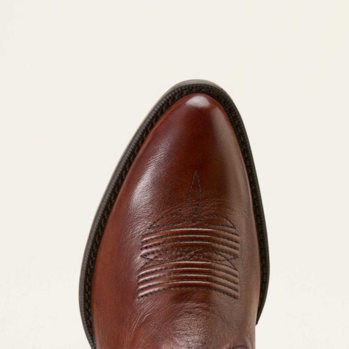 Close-up of a brown leather r toe boot with stitching detail on a beige background.
