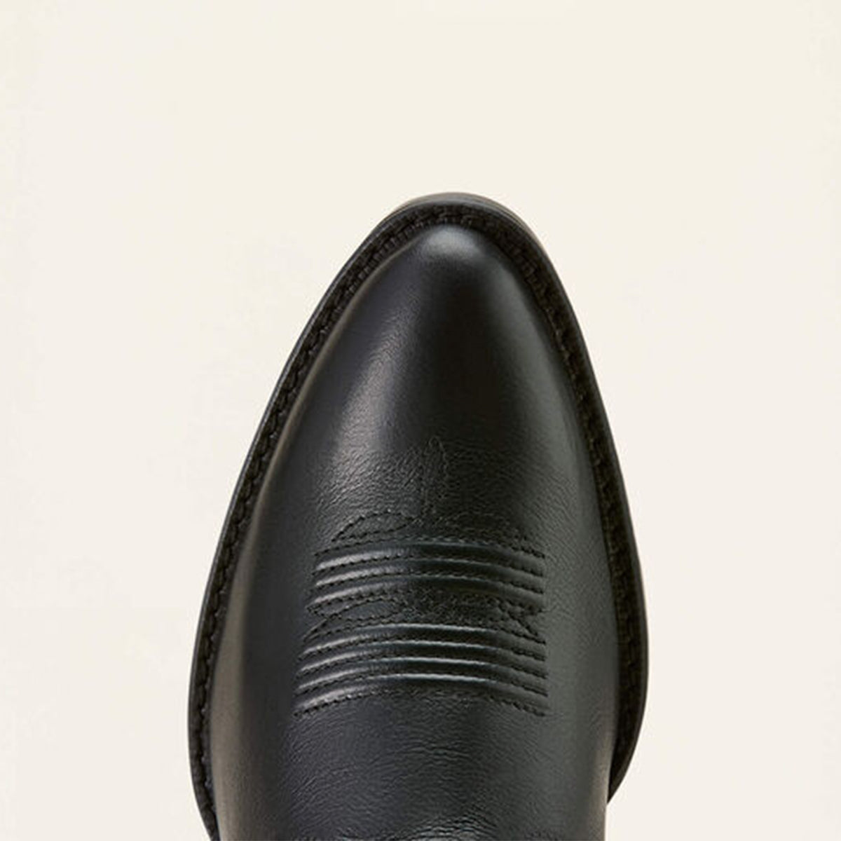 Close-up of a Ariat black leather boot toe on a beige background.