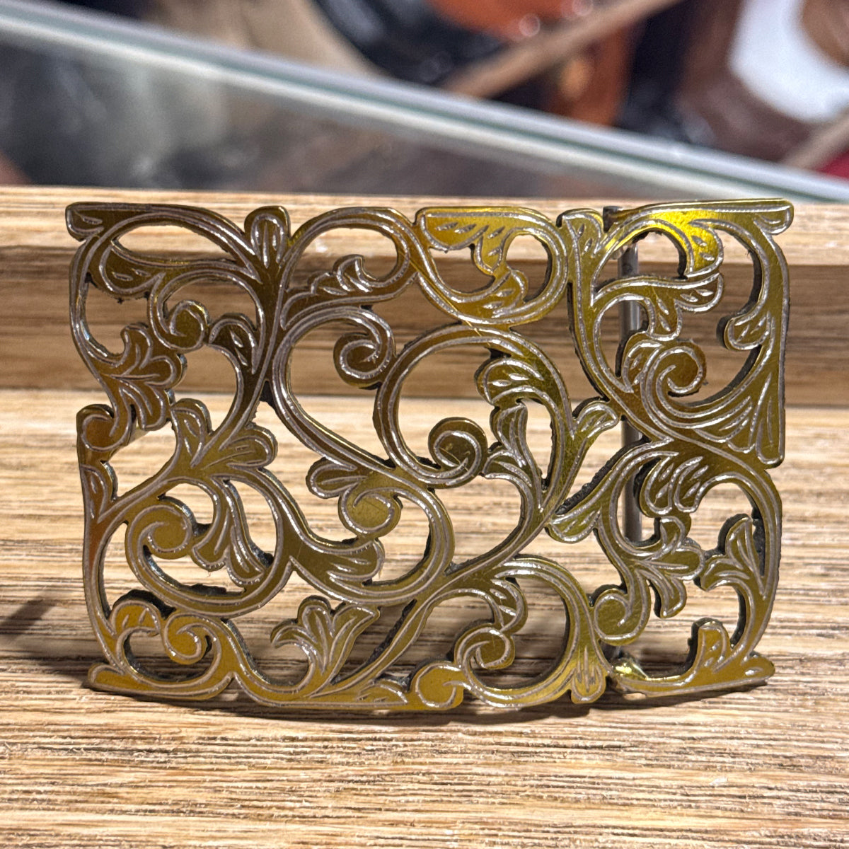 In-store counter display view of the handcrafted gold-tone stainless steel belt buckle shown on a wooden display.