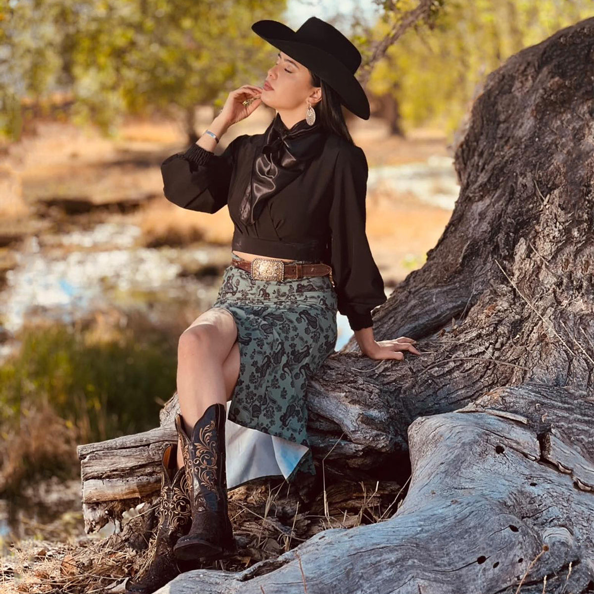 Women sitting on a tree while wearing a Cowgirl outfit.