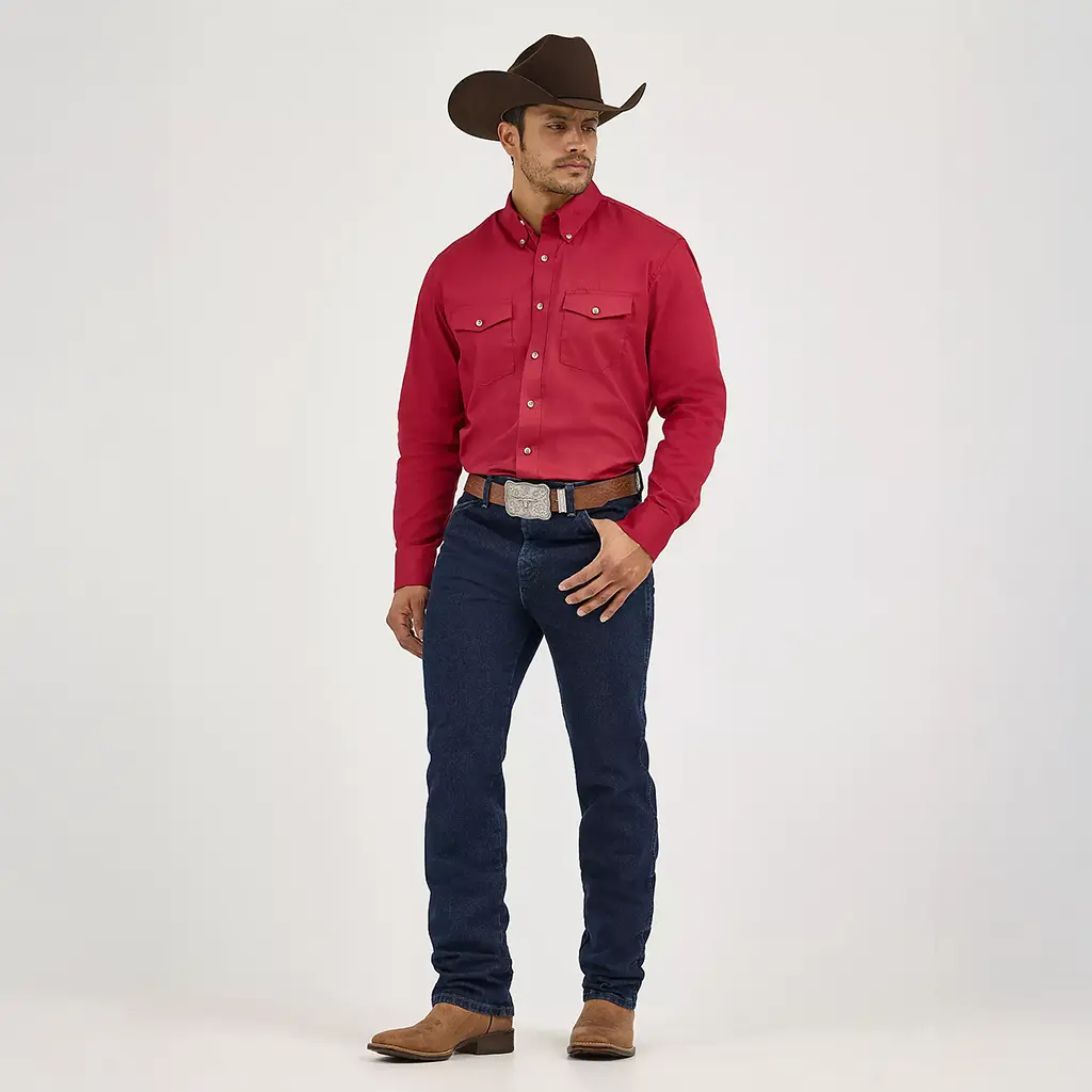 Full-length studio hero shot of a model wearing Wrangler Men's Dark Stone Cowboy Cut Slim Fit jeans styled with a red Western shirt, brown belt, and cowboy hat.