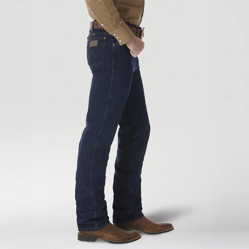 Side profile view of a model wearing the Wrangler 0936DSD Dark Stone jeans displaying the slim fit leg over brown leather boots.