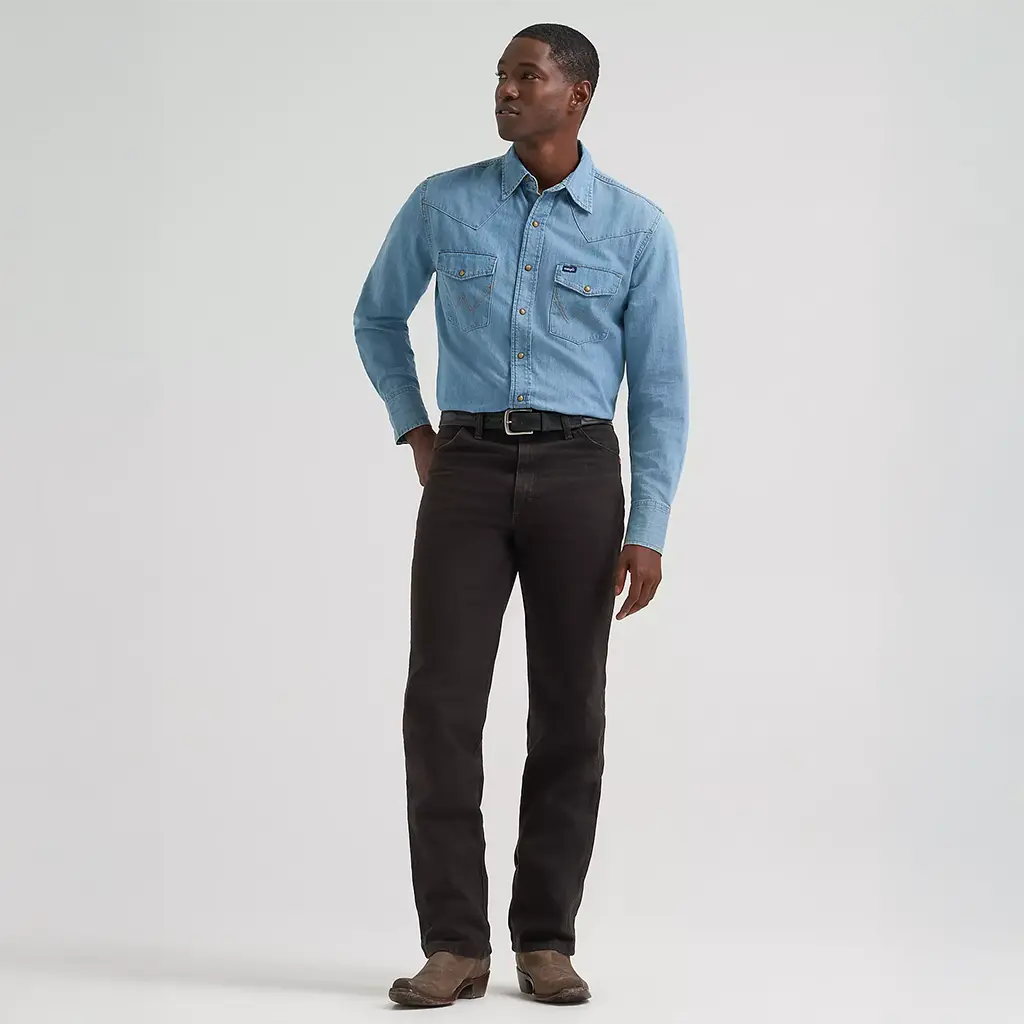 Full-length studio view of a model wearing Wrangler Men's Black Chocolate Cowboy Cut Slim Fit jeans paired with a denim Western shirt and brown boots.