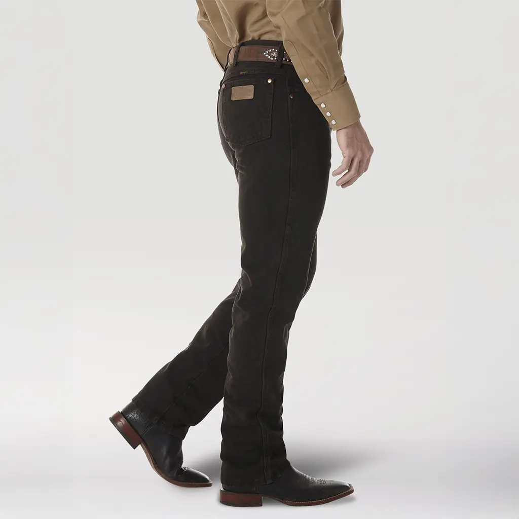 Side profile studio view of a model wearing the Wrangler 0936KCL Black Chocolate jeans displaying the slim fit leg over cowboy boots.