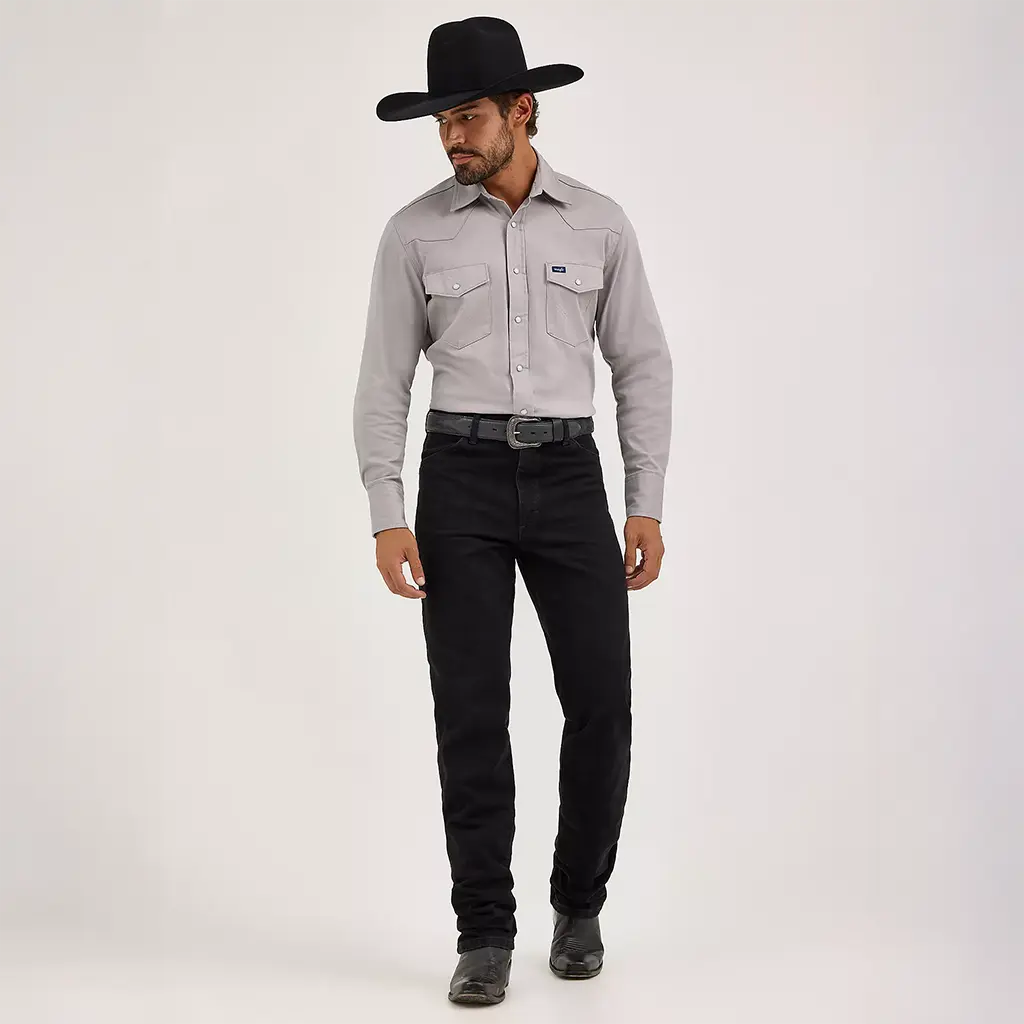 Full-length studio view of a model wearing Wrangler Men's Shadow Black Cowboy Cut Slim Fit jeans styled with a grey Western shirt, black belt, and black cowboy hat.