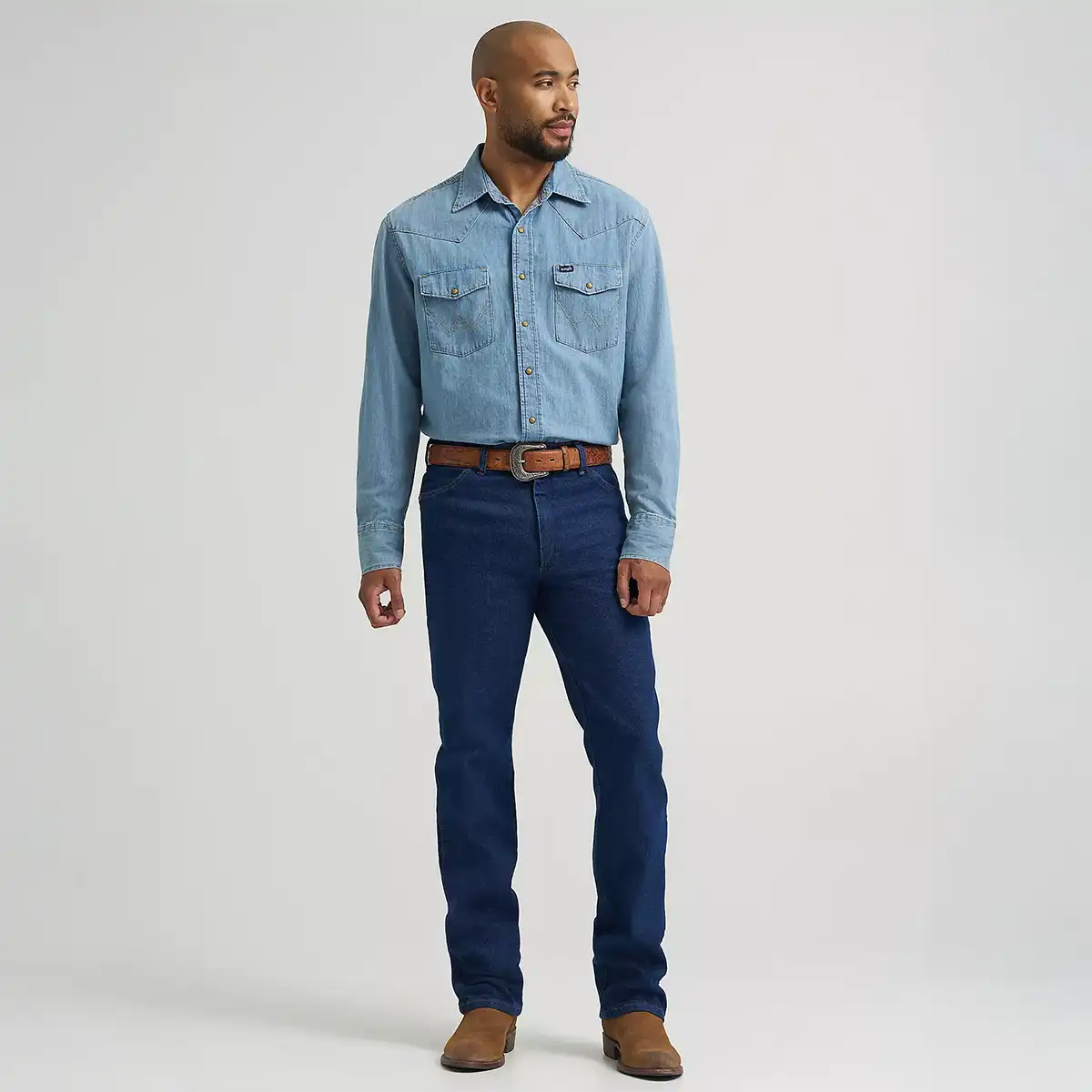 Full length front view of a man wearing Wrangler Men's Cowboy Cut navy stretch slim fit jeans with denim shirt and boots.