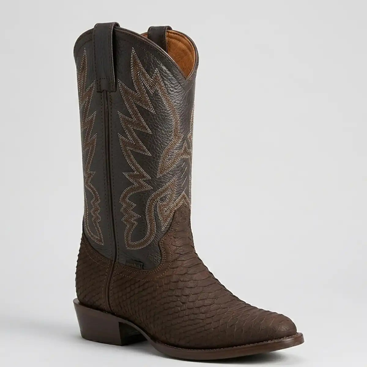 A single brown western cowboy boot with a textured python print lower section, dark brown shaft, and tan/light brown embroidered stitching, shown against a light gray background.