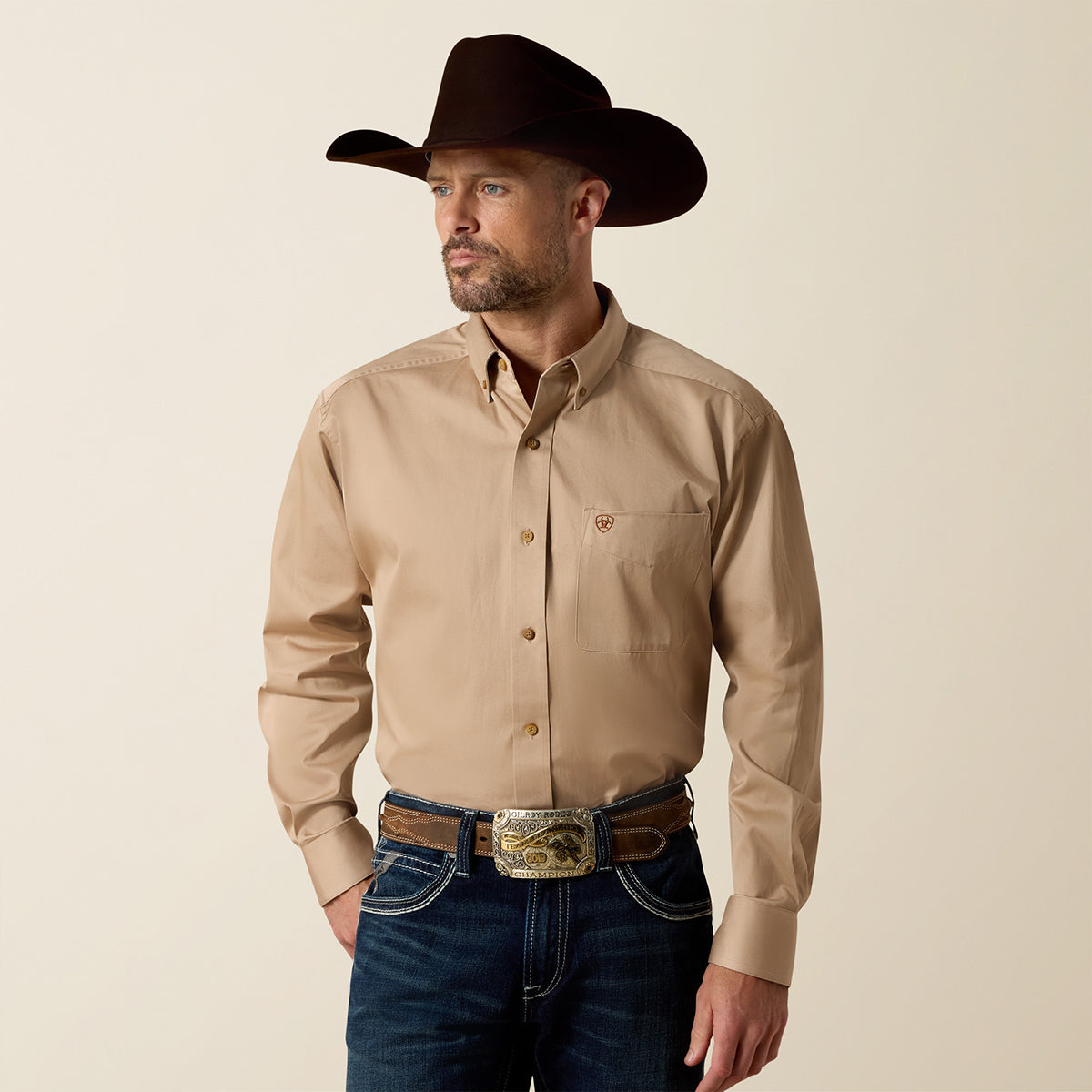 Front view of a man wearing the Ariat Men's Solid Twill Khaki long sleeve button-down shirt with dark jeans, belt buckle, and cowboy hat.