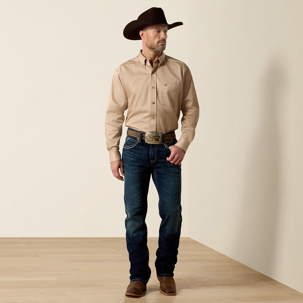 Front and full-body view of a man wearing the Ariat Men's Solid Twill Khaki long sleeve button-down shirt with dark jeans, belt buckle, and cowboy hat.