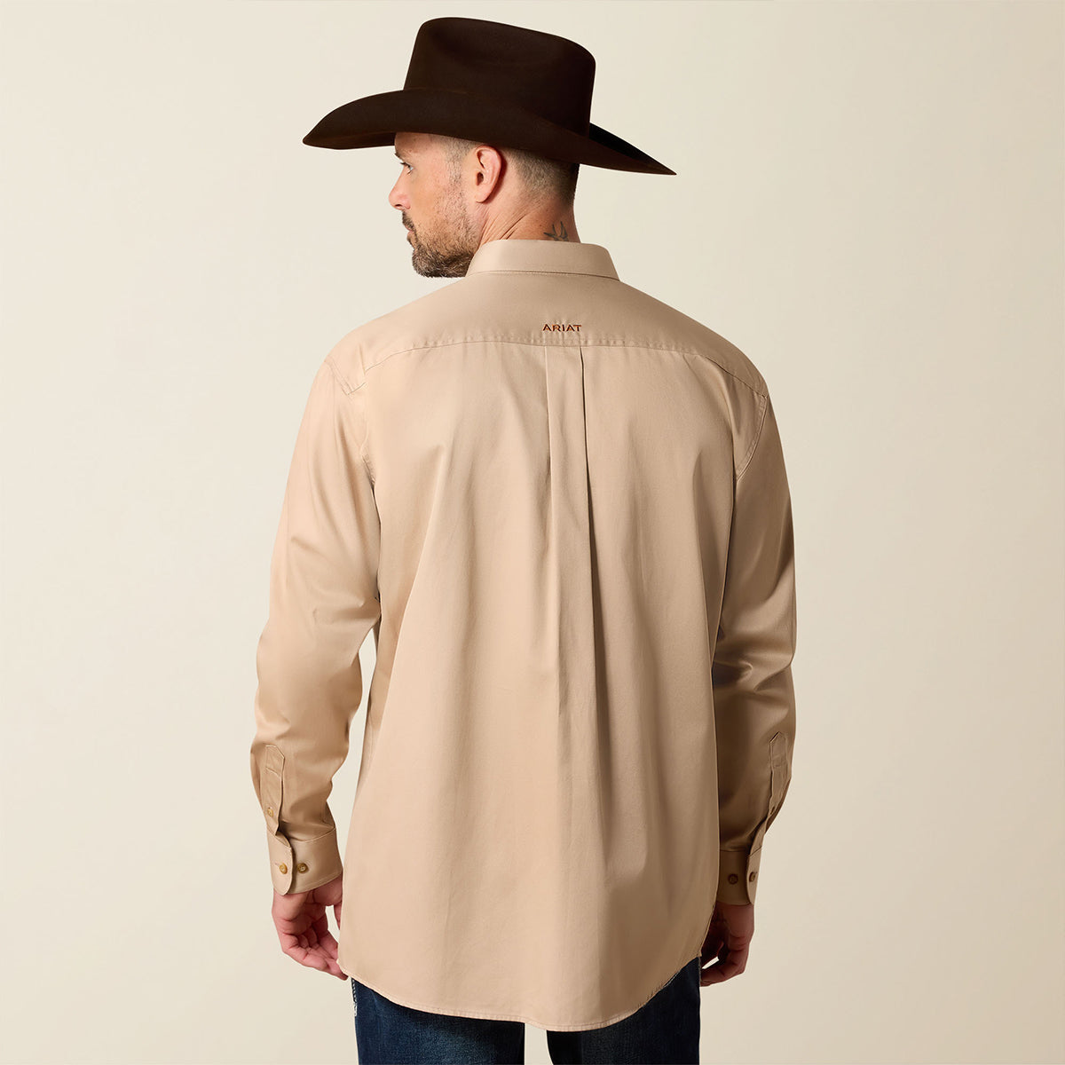 Man wearing a Ariat beige shirt and dark cowboy hat on a beige background