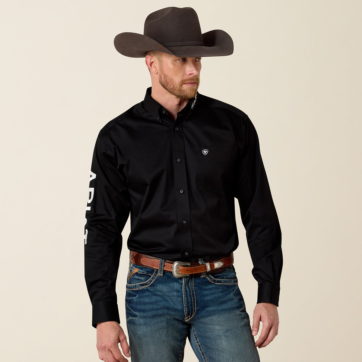 Front view of a man wearing the Ariat Men's Black Team Logo long sleeve twill shirt with white sleeve and collar embroidery.